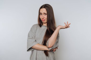 Woman in gray shirt shrugging with one hand raised