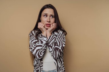 A woman with long dark hair looks worried, wearing a zebra-striped shirt against a beige background.