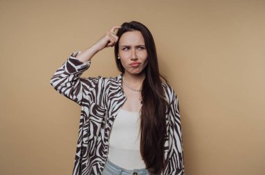 Woman scratching her head in confusion against a beige background.