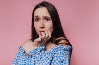A worried woman in a blue checkered dress against a pink background.