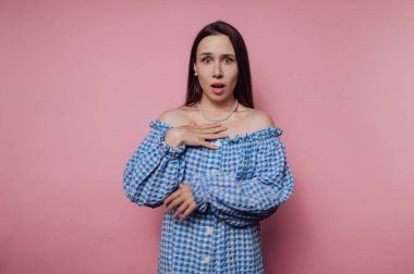 Surprised woman in blue checkered dress against pink background.