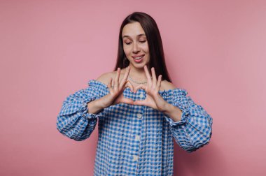 Woman in blue checkered dress making heart shape with hands.