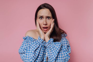 Woman in blue checkered top with surprised expression on pink background.