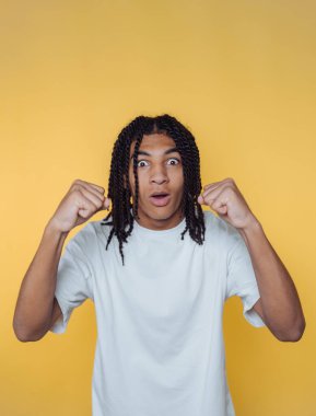 Surprised young man with raised fists against yellow background.
