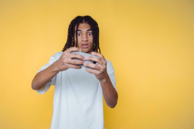 Young man with dreadlocks playing video games, yellow background.