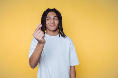 A young person with braided hair making a hand gesture against a yellow background