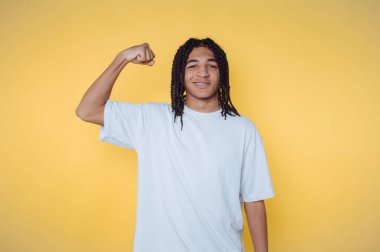 Young person flexing arm in a white t-shirt against yellow background.