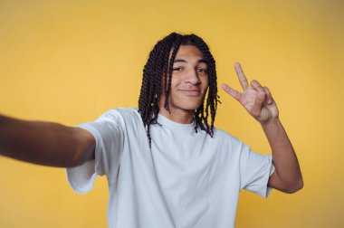 Young man taking a selfie with a peace sign on a yellow background.