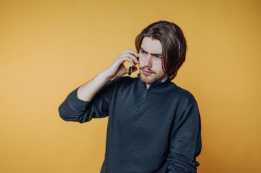 Young man with long hair talking on a smartphone against a yellow background.
