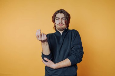 Man in black sweater making a hand gesture against orange background.