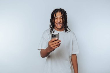 Young man with braided hair smiling while looking at smartphone.