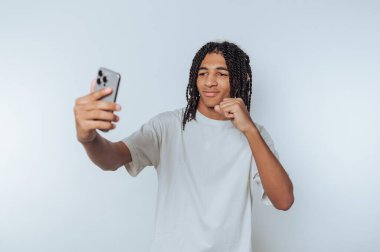 Young man with braided hair taking a selfie against a white background.