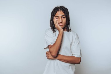 Young person with braided hair in a white shirt looking bored.