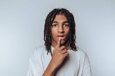 Young man with finger on lips, thoughtful expression.