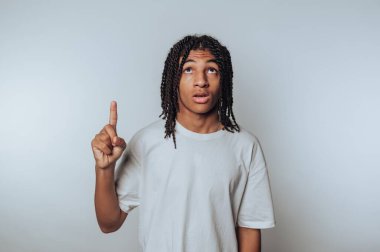 Young man with dreadlocks pointing upward, looking curious.