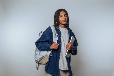 Young man with backpack and laptop, casual attire, neutral background.