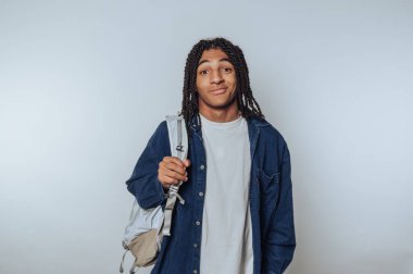 Young man with dreadlocks holding a backpack, wearing casual clothes.