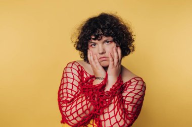 Person with curly hair in red netted top against yellow background.