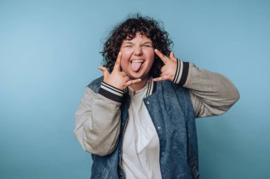 Person with curly hair making a playful gesture against blue background.