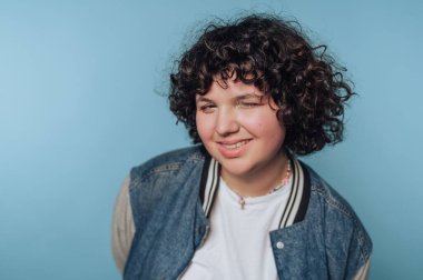 Smiling person with curly hair winking against a blue background.