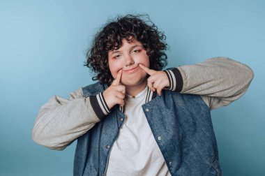 Mavi arka planda kot ceketli, kıvırcık saçlı, gülümseyen biri..