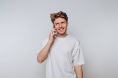 Young man in white t-shirt talking on smartphone, smiling.