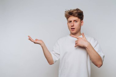Young man in white t-shirt gesturing with surprise against gray background.