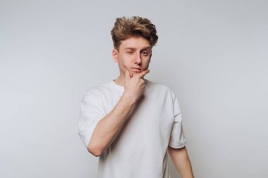 Young man in white t-shirt winking and touching chin