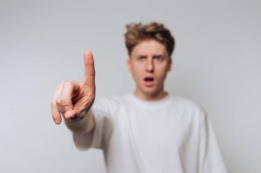 Young man in white shirt pointing with surprised expression.