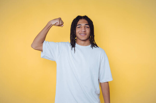Young person flexing arm in a white t-shirt against yellow background.