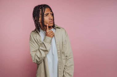 Genç bir adamın portresi düşünceli bir şekilde yana bakıyor, hızlı bir ifadeyle, pembe arka plandaki belirsizliği ve merakı yansıtıyor.