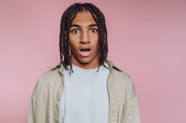 Şaşırmış genç bir adamın portresi pembe arka planda şok olmuş bir ifadeyi gösteriyor.