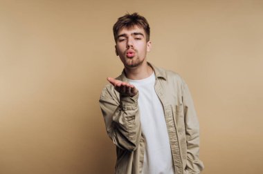 Öpüşen genç adamın portresi, bej arka planda sevgi ve neşe dolu neşeli bir anı yakalıyor.