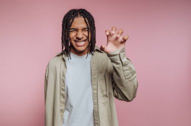 Genç bir adamın portresi bir pençe jestini büyük bir gülümsemeyle gösterir. Pembe arka planda coşku ve enerjiyi somutlaştırır.