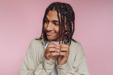 Genç oyuncu portresi gülümserken saçlarını nazikçe tutuyor, pembe arka planda rahat bir pozla.