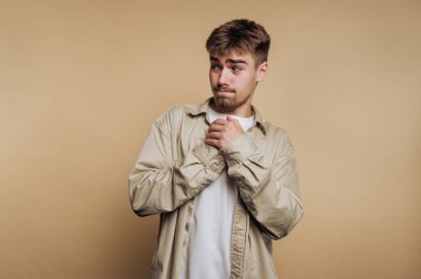 Düşünceli bir ifadeyle genç bir adamın portresi bej arka planda ellerini bir arada tutuyor.