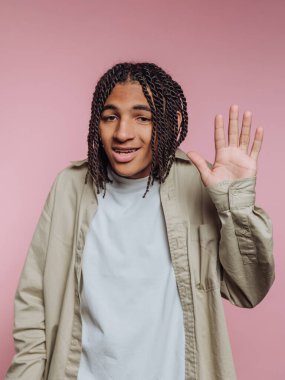 Gülümseyerek el sallayan genç bir adamın portresi pembe arka planda dostluk gösterisi yapıyor.