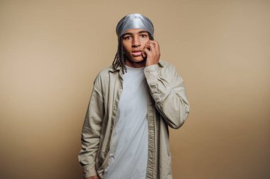 Düşünceli genç bir adamın portresi, eli yanağında, bej arka planda merak ve içgözlem duygusunu iletiyor.