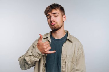 Genç adamın portresi Shaka 'ya el hareketi yapıyor, beyaz arka planda güven ve rahatlama gösterirken rahat bir hava yayıyor.