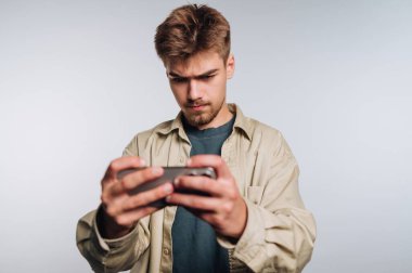 Akıllı telefonuyla oyuna dalmış genç bir adamın portresi, beyaz arka plandaki konsantrasyonu ve keyfi gösteriyor.
