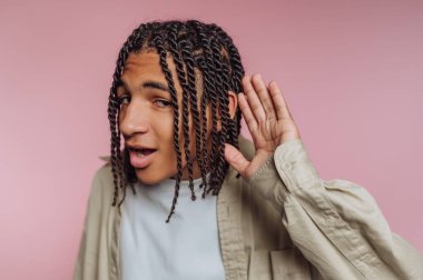 Saçları örgülü genç bir adamın portresi kulağını çekerken, pembe arka planda merakını ve nişanını sergiliyor.