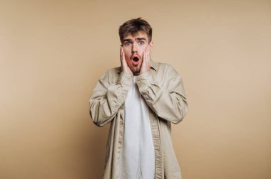 Şaşırmış genç adamın portresi, bej arka plandaki insan tepkilerini vurguluyor.