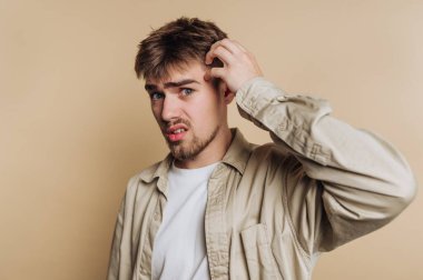 Kafasını kaşıyan genç adamın portresi bej arka planda kafa karışıklığını gösteriyor.