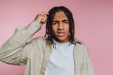 Saçları örgülü genç bir adamın portresi derin düşüncelere dalmış, pembe arka planda karışık bir ifade sergiliyor.