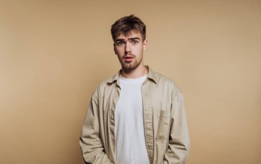 Bej arka planda nötr bir yüz ifadesiyle şaşıran genç bir adamın portresi
