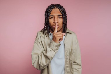 Genç bir adamın portresi, parmaklarıyla dudaklarında, bir sessizlik jesti ve pembe arka plan üzerine tefekkür yapıyor.