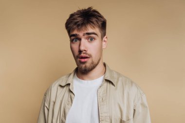 Genç adamın portresi şaşırtıcı bir ifadeyi bej arka planda somut bir şok ve merak gösteriyor.