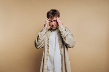 Genç bir adamın portresi, başını tutup bej arka planda duygusal bir an yakalayarak hayal kırıklığını ifade eder.