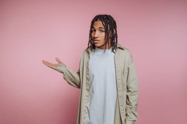 Genç bir adamın portresi düşünceli bir ifadeyle gelişigüzel poz veriyor, pembe arka planda vücut dili yoluyla duygularını gösteriyor.