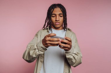 Genç bir adamın portresi, bir akıllı telefon kullanırken derinden odaklanmış görünüyor. Nişanı ve pembe arka plan üzerindeki konsantrasyonunu gösteriyor.